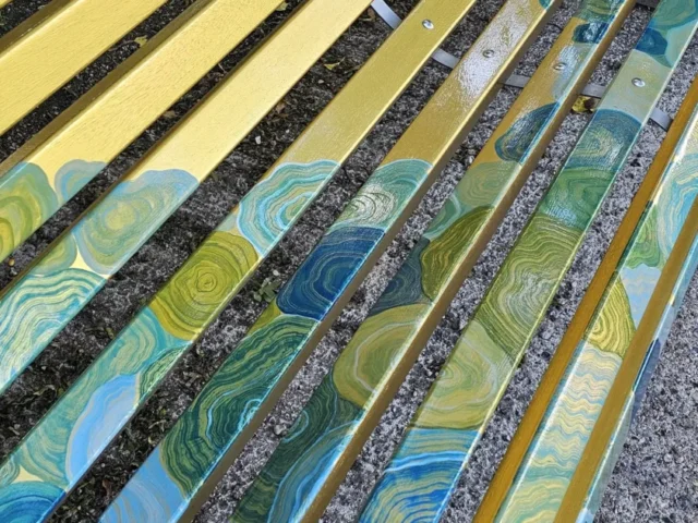 Glossy gold, blue and green painted timber slats showing the protected finish on the River Lea Art Trail bench.